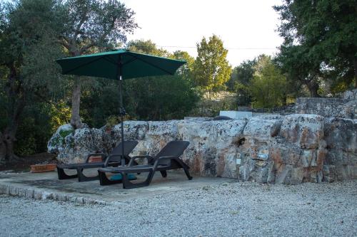 two chairs and an umbrella next to a rock wall at Trullo Fortuna in Cisternino