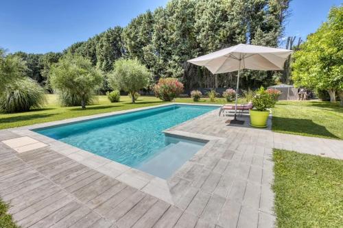 une piscine dans une cour avec un parasol dans l'établissement La Villa aux Cyprès bleu, au Thor