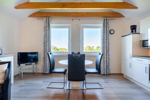 a dining room with a table and chairs and two windows at Ferienwohnung Ebbe mit Loggia und schönem Ausblick am Badesee Tannenhausen in Aurich