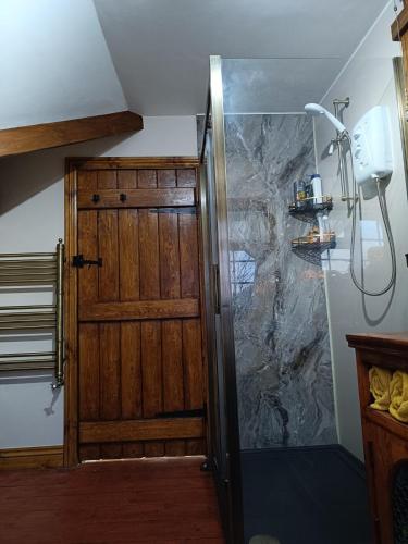 a shower with a wooden door in a bathroom at A peaceful cottage in the countryside in Abermule