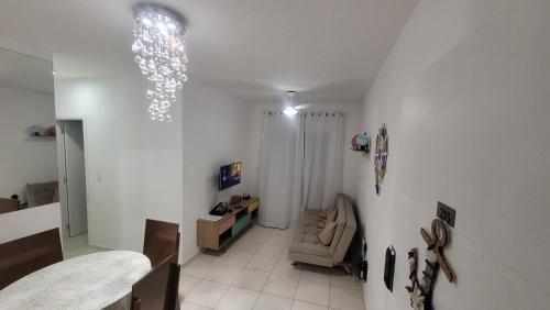 a white living room with a couch and a chandelier at Confortável apartamento perto de praias - Bertioga in Bertioga