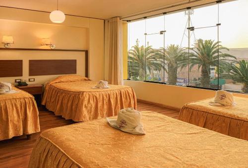 a hotel room with three beds and a large window at HOTEL AVENIDA in Tacna