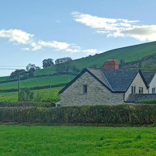 a stone house in the middle of a green field at A peaceful cottage in the countryside in Abermule