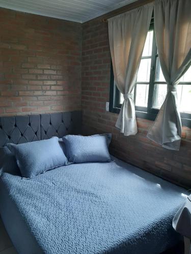 a bed in a bedroom with a brick wall and windows at Canto do Beija-flor Rolante RS in Rolante