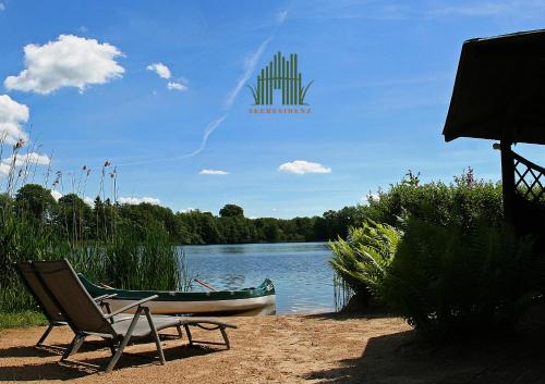 a chair and a boat on the shore of a lake at Ferienhaus SEERESIDENZ am Mühlensee in Godern
