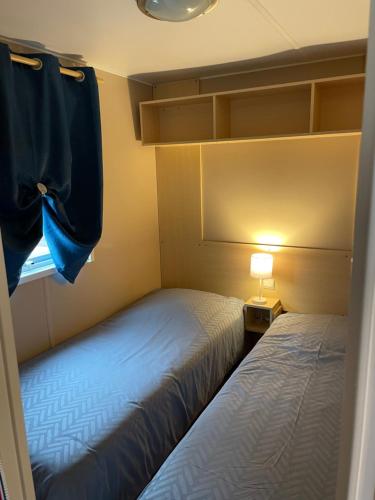 two beds in a room with a window and a lamp at 600m de la plage - Mobilhome Loka 4 personnes camping Goelands 3 étoiles in Saint-Martin-Plage