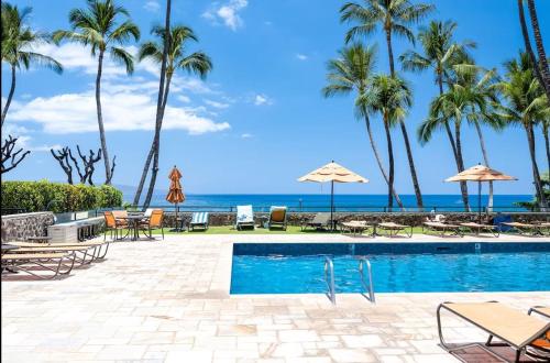 a swimming pool with palm trees and the ocean at Wailea Elua Resort 1904 in Wailea