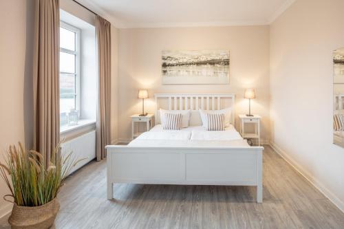 a white bedroom with a white bed and two windows at Austernfischer in Westermarkelsdorf