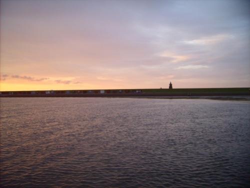 einen Sonnenuntergang über dem Wasser mit einem Leuchtturm in der Ferne in der Unterkunft Haus Halligblick, Ferienwohnungen am Wattenmeer, Whg Oland in Dagebüll