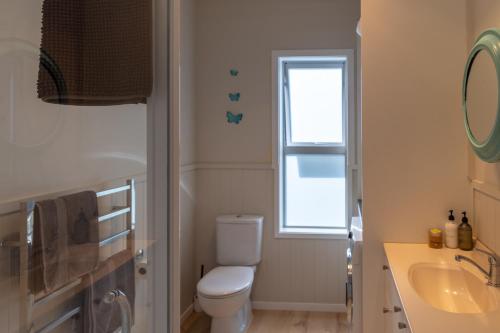 a bathroom with a toilet and a sink and a window at Tūī Guesthouse in Cooks Beach