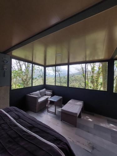 a bedroom with a bed and a couch and windows at Arenal volcano apartment with panoramic view in El Castillo de La Fortuna