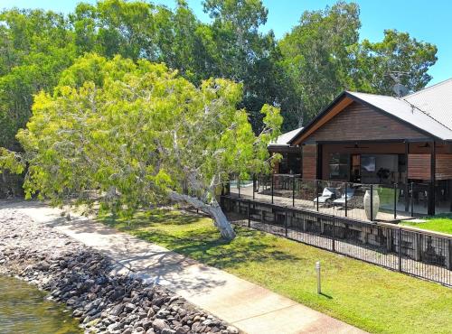 a log cabin with a tree next to a body of water at Lake House, stroll to beach & cafes- Pets Welcome in Trinity Beach