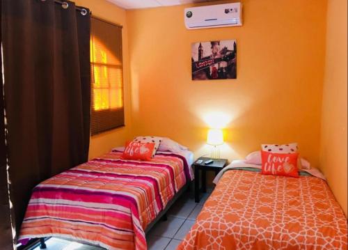 two beds in a room with orange walls at Casa central in San Juan del Sur