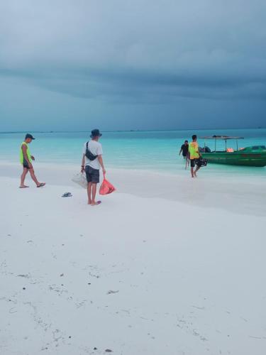 a group of people walking on a beach with a boat at Amaro Homestay in Nuhu Tawun