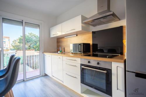 une cuisine avec des placards blancs et une grande fenêtre dans l'établissement Le coin des agrumes Jardin Proche Centre Ville, à Perpignan