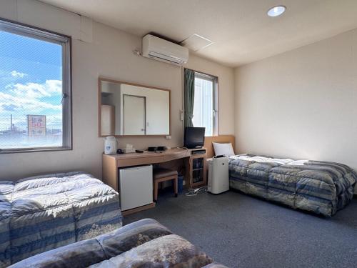 a room with two beds and a desk with a computer at Business Hotel Okadaya Toyohashi in Toyohashi