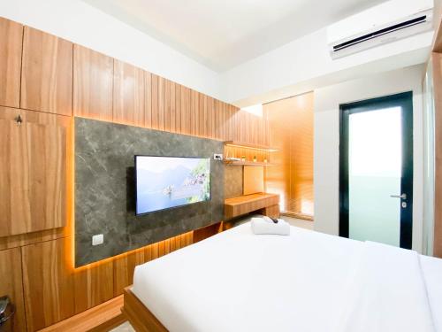 スマランにあるCozy and Tidy 1BR The Alton Apartment By Travelioのベッドと壁掛けテレビのある寝室