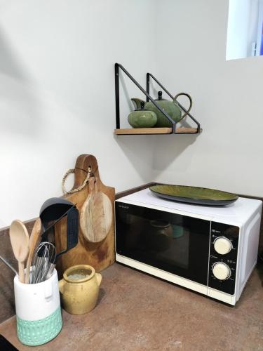 un four micro-ondes assis sur un comptoir avec d'autres ustensiles de cuisine dans l'établissement Maison de pêcheur en bord de mer, à Grandcamp-Maisy