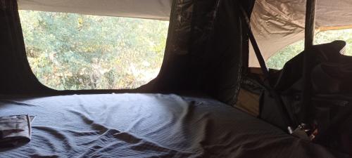 a bed in the back of a tent with a window at Tente Perchée Kenya MAS DE BOUZOU in Grèzes