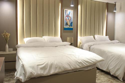 two beds with white sheets in a room at Azmal Hotel & Suites in Irbid