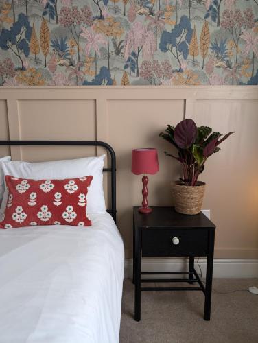 a bed with a red pillow and a table with a lamp at Rooms At The Rosebery in Norwich