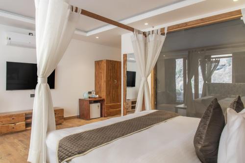 a bedroom with a bed with curtains and a television at Echor Palm Bliss Riverside Resort & Spa Kasol in Kasol