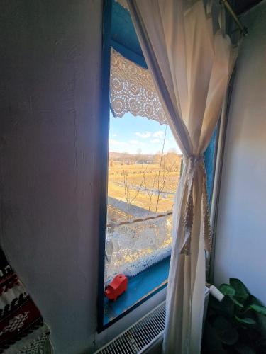 a window with a curtain and a view of a field at Complex Tradițional Casa din Vale Breb in Breb