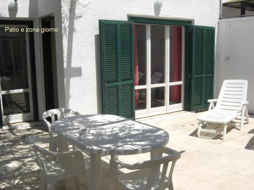 a table and chairs on a patio with green shutters at Casetta nel Villaggio Conca Specchiulla in Conca Specchiulla