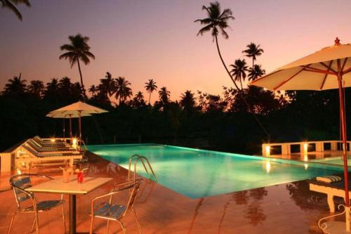a pool with a table and chairs and an umbrella at Abad Turtle Beach in Mararikulam