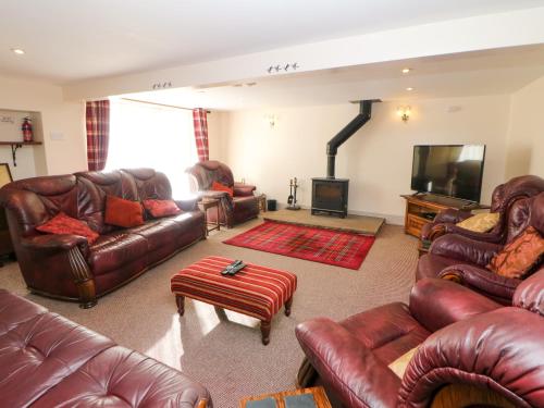 a living room with leather furniture and a fireplace at Ford Coach House Cottage in Leek
