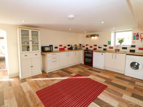 a large kitchen with white cabinets and a red rug at Ford Coach House Cottage in Leek