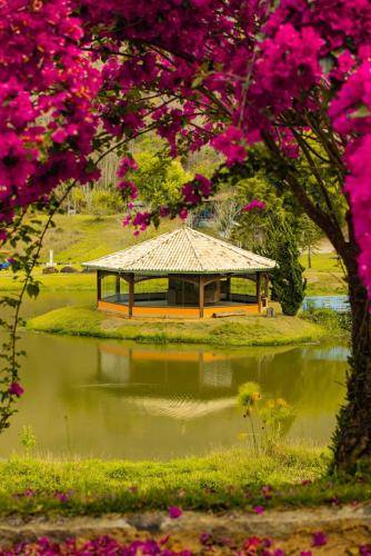 a gazebo in a park with a pond and flowers at Hotel Fazenda Jecava in Campanha