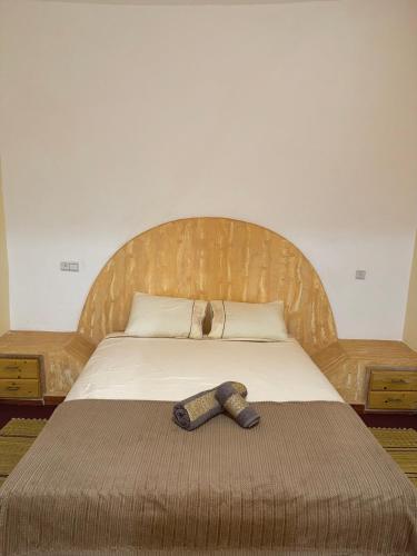 a bed with a wooden headboard with a tie on it at Hôtel Khalwa in Jenane Sidi Amer