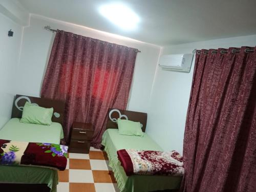 a bedroom with two beds and red curtains at الشريف للشقق الفندقيه in Abu Simbel