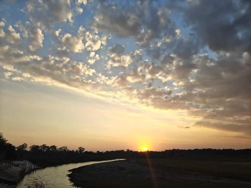 a river with the sun setting in the sky at Amantran Hotel & Resort, Chilapata in Patkapāra