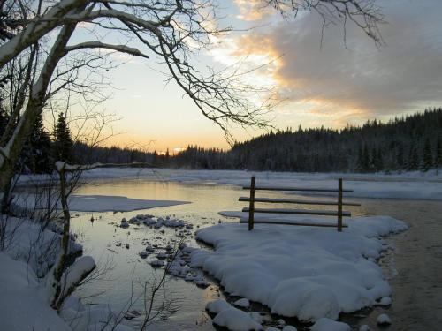 a bench sitting in the snow next to a river at The Old Logging Camp in Yttermalung