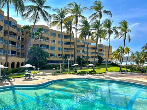 a swimming pool with palm trees in front of a resort at Apto Vip acceso a la playa in El Morro de Barcelona