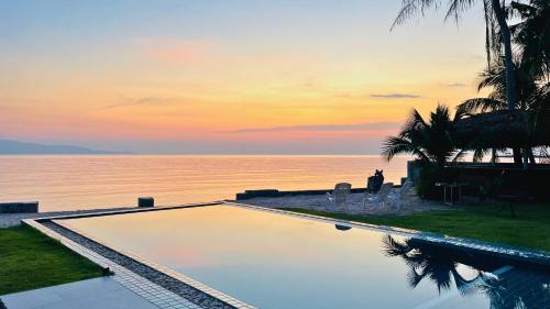 a swimming pool with a view of the ocean at sunset at The White House Beach Apartments Koh Phangan in Ban Nua