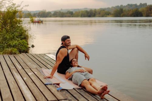 a man and woman sitting on a dock on a lake at AZUR Camping Regensburg in Regensburg