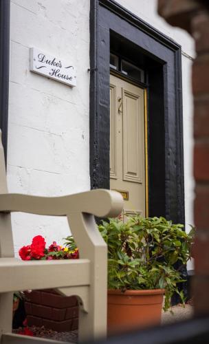 a white building with a door and a bench and flowers at Duke's House, Penrith - Stunning Large Home - Town Centre on your Doorstep - 5 Bedrooms & Sun Trap Garden - Lake District Stay in Penrith