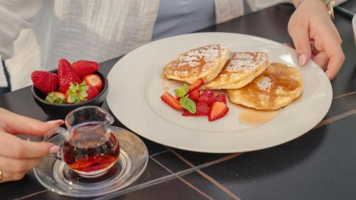a person holding a plate of pancakes and strawberries at The Abdali Boulevard Hotel in Amman
