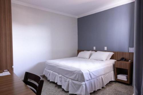 a bedroom with a large white bed and a chair at BOMBONATO HOTEL - Fácil Acesso ao Aeroporto e parque de Exposições ABCZ in Uberaba