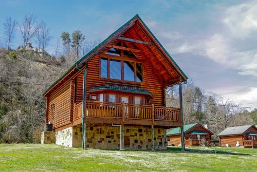 a log cabin with a deck on a grass field at River Cabin in Pigeon Forge