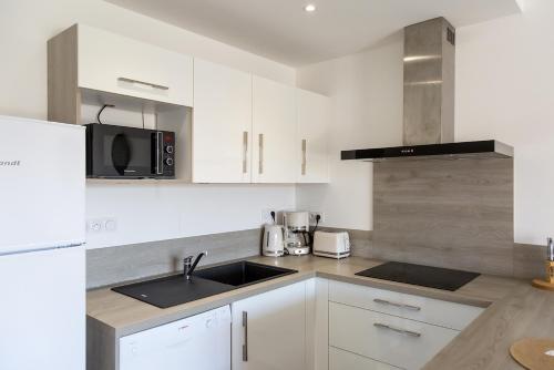 une cuisine blanche avec un évier et un micro-ondes dans l'établissement Résidence Domaine d'Arca Porto Vecchio - T2 haut standing - 4 personnes 