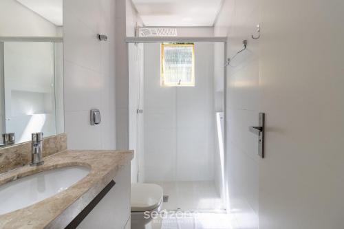 een witte badkamer met een wastafel en een douche bij Apto Vista Mar 240m da Praia em Jurerê IDO207 in Florianópolis
