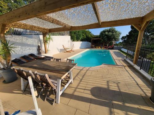 une terrasse avec une table en bois et une piscine dans l'établissement Belle Villa au calme avec Piscine grands volumes à deux pas des plages de La Ciotat, à La Ciotat