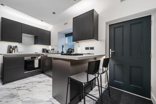 a kitchen with black cabinets and a bar with stools at Modern Town House In Cockermouth in Cockermouth