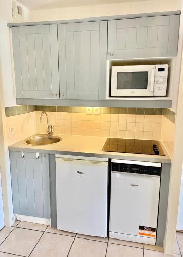 une cuisine avec des armoires blanches, un évier et un micro-ondes dans l'établissement BISCARROSSE Charmant T2 Au cœur du Golf avec piscine Entre Lac & Océan - Ménage inclus, à Biscarrosse