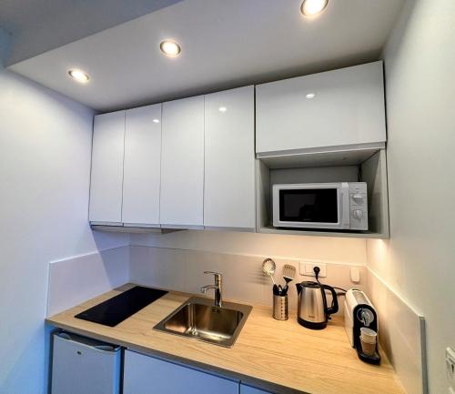 a kitchen with white cabinets and a sink and a microwave at Troyes - Aux pieds du cube in Troyes