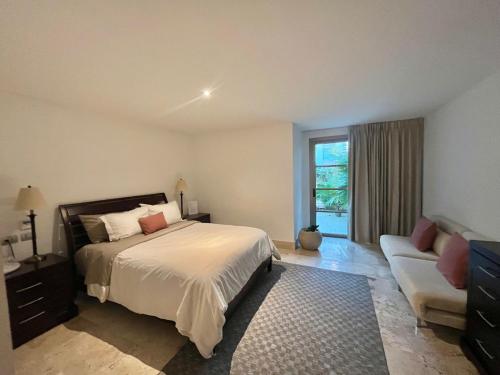 a bedroom with a bed and a couch and a window at Departamento exclusivo con playa privada - La Amada, Cancun in Cancún